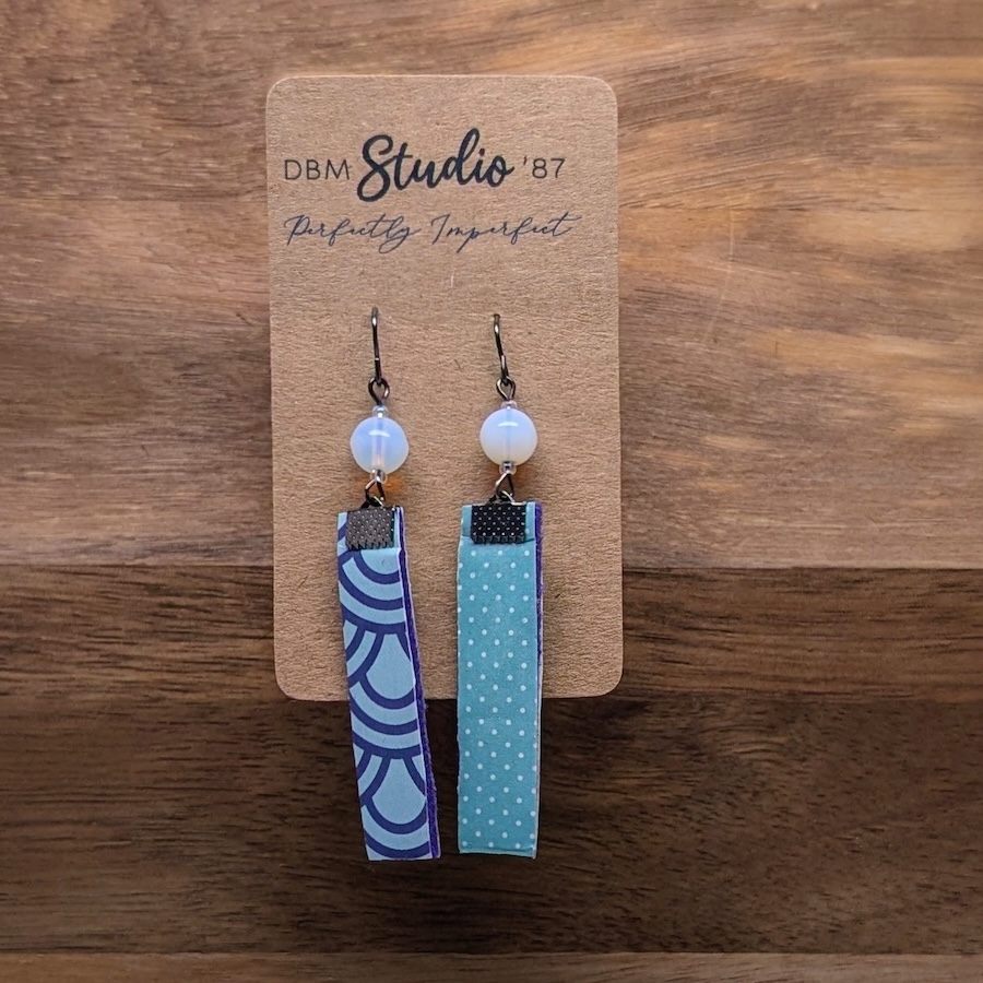 Medium length scrapbook earrings rectangles with purple felt core. Front is Light blue with purple swirls. Back is Light blue polka dots. Light blue/peal beads and pewter-toned metals. Back a